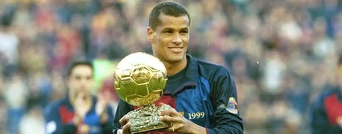 Soccer player in navy and blue jersey holding gold trophy on field, premium sports fashion style