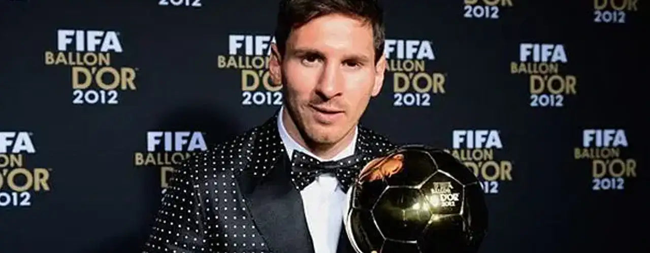 Soccer player in a polka dot suit holding Ballon d'Or trophy at FIFA 2012 awards backdrop