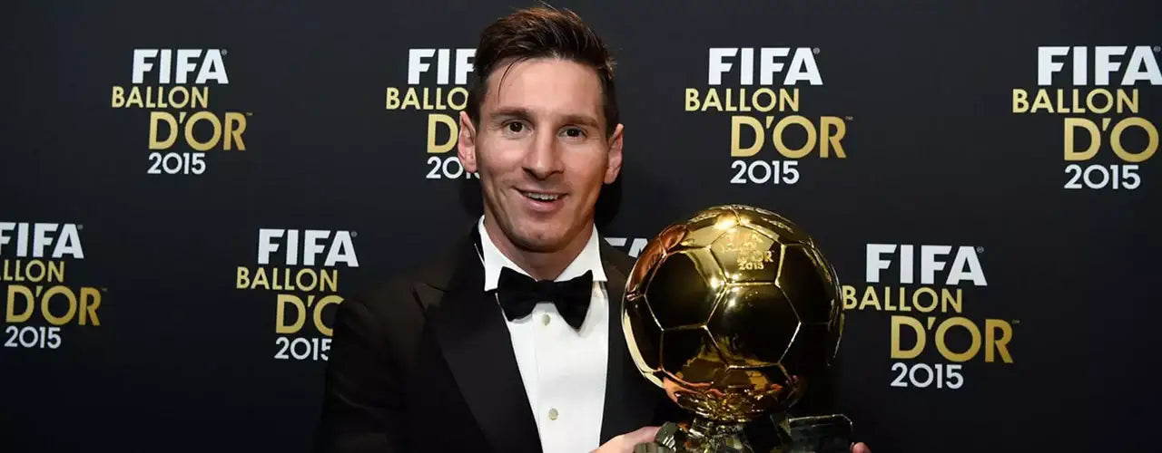 Soccer player in tuxedo holding FIFA Ballon d'Or 2015 trophy at awards event backdrop