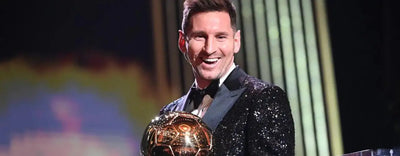 Smiling athlete in a black sequined tuxedo holding a gold sports trophy at an awards event