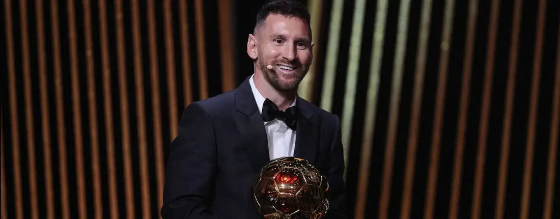 Man in a black tuxedo holding a golden soccer trophy on a dark stage, sports fashion inspiration