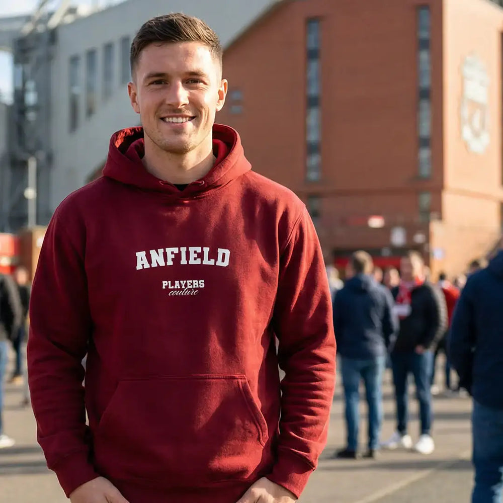 Man wearing maroon Anfield Players Couture hoodie outside stadium, casual sports fashion style