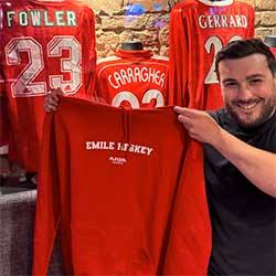 Person holding a red sports jersey with 'Emile Heskey' printed on it, surrounded by other Liverpool FC jerseys.